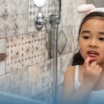 A young child checking their teeth in a bathroom mirror